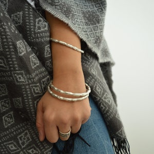 Puede incluir: Un conjunto de tres pulseras de plata con textura martillada. Las pulseras se llevan en la muñeca.