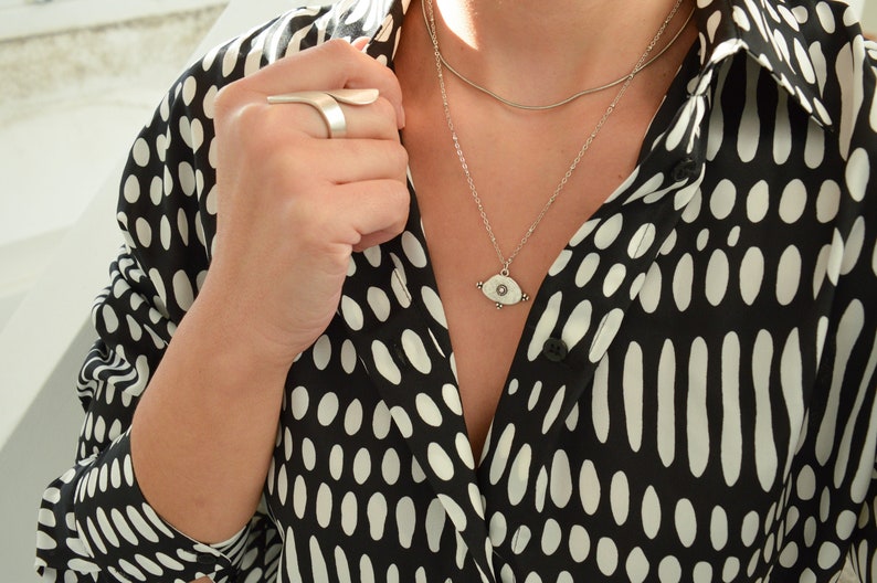 May include: A silver necklace with a white eye pendant on a black and white polka dot shirt.