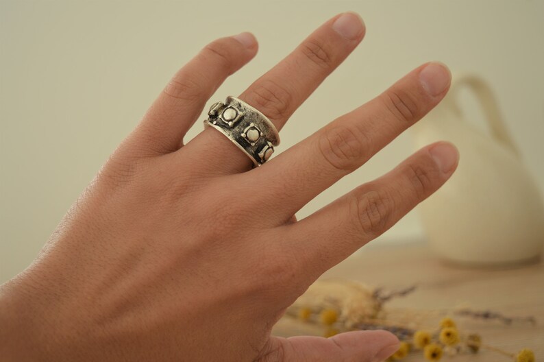 May include: A silver ring with a wide band and a row of raised squares with small circles in the center.