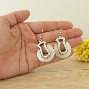 May include: A pair of silver hoop earrings with a unique, abstract design. The earrings are made of metal and have a smooth, polished finish.