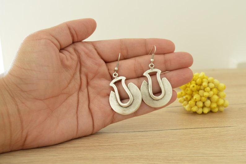 May include: A pair of silver hoop earrings with a unique, abstract design. The earrings are made of metal and have a smooth, polished finish.