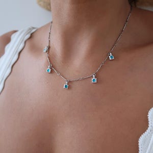 May include: A silver chain necklace with five turquoise square pendant charms.