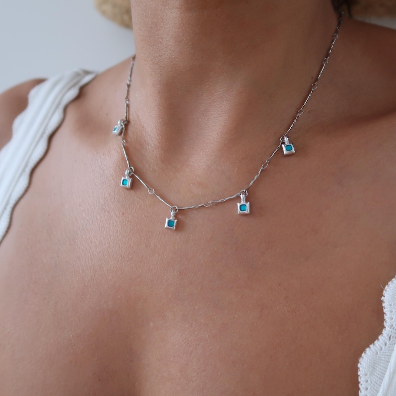 May include: A silver chain necklace with five turquoise square pendant charms.