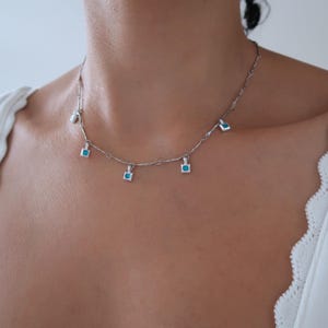 May include: A silver chain necklace with five small square pendants, each featuring a turquoise blue gemstone.