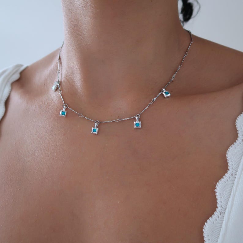 May include: A silver chain necklace with five small square pendants, each featuring a turquoise blue gemstone.