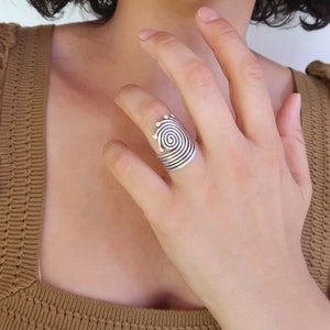 Op de afbeelding: Een zilveren ring met een spiraalvormig ontwerp. De ring wordt gedragen aan de wijsvinger van een hand.