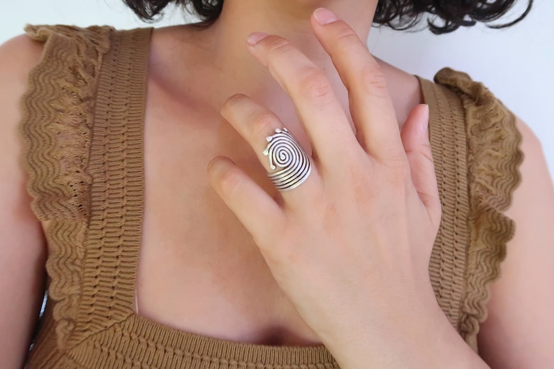 Op de afbeelding: Een zilveren ring met een spiraalvormig ontwerp. De ring wordt gedragen aan de wijsvinger van een hand.