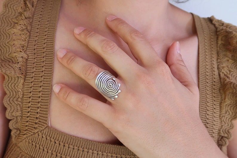 Op de afbeelding: Een zilveren ring met een spiraalvormig ontwerp. De ring wordt gedragen aan de wijsvinger van een hand.