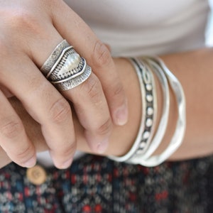 Puede incluir: Un anillo de plata con un diseño texturizado y un centro elevado. El anillo se lleva en un dedo.