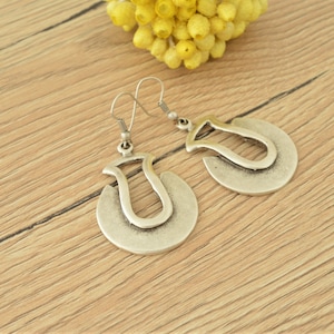 May include: A pair of silver earrings with a unique, abstract design. The earrings are shaped like a crescent moon with a smaller, curved shape inside.