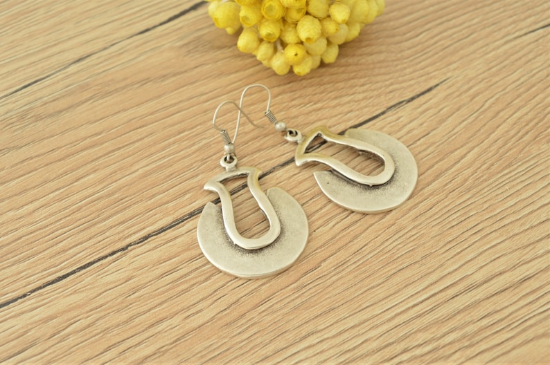 May include: A pair of silver earrings with a unique, abstract design. The earrings are shaped like a crescent moon with a smaller, curved shape inside.