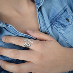 May include: A silver ring with an eye design. The ring is open and adjustable.