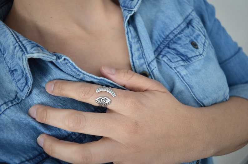 May include: A silver ring with an eye design. The ring is open and adjustable.