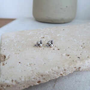 May include: A pair of silver bee stud earrings with detailed wings and a textured body.
