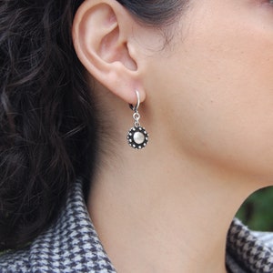 May include: Silver hoop earrings with a round, silver charm featuring a textured, circular design with a raised center.