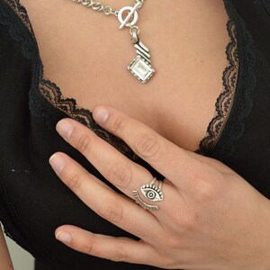 May include: A silver ring with an eye design. The ring is adjustable and can be worn on any finger.
