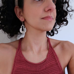 May include: Silver earrings with a unique, abstract design. The earrings are made of two overlapping circles, with a cutout in the shape of a teardrop in the center of the larger circle.