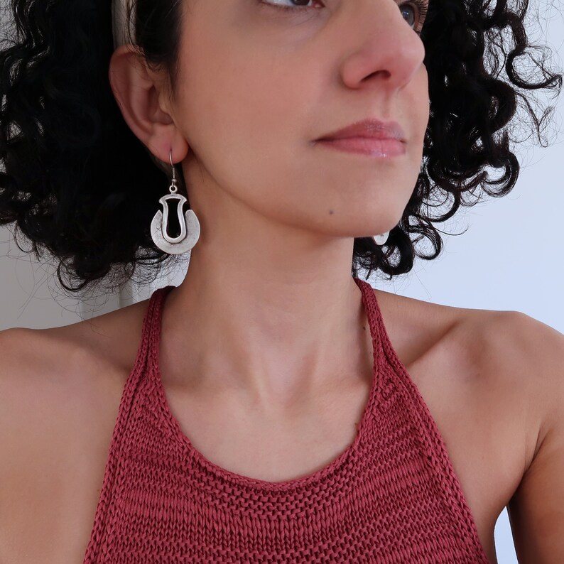 May include: Silver earrings with a unique, abstract design. The earrings are made of two overlapping circles, with a cutout in the shape of a teardrop in the center of the larger circle.