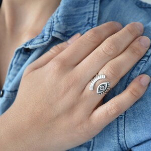 May include: A silver ring with an eye design. The ring is open and adjustable.