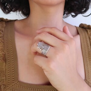 Op de afbeelding: Een zilveren ring met een spiraalvormig ontwerp. De ring wordt gedragen aan de wijsvinger van een hand.