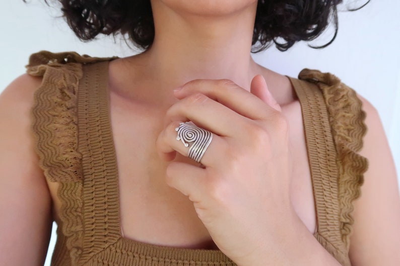 Op de afbeelding: Een zilveren ring met een spiraalvormig ontwerp. De ring wordt gedragen aan de wijsvinger van een hand.