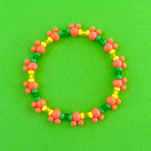 Peut inclure: Un bracelet en perles colorées avec des perles orange, jaunes et vertes alternées. Les perles sont disposées en un motif de trois perles de chaque couleur.