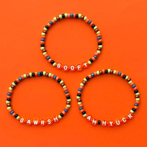Peut inclure: Trois bracelets en perles colorées avec les mots "GOOFY", "GAWRSH" et "AH HYUCK" écrits en lettres blanches.