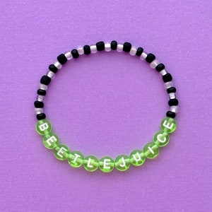 May include: A green and black beaded bracelet with the word "BEETLEJUICE" spelled out in white letters.