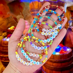 May include: Seven colorful beaded bracelets with the names "Sneezy", "Bashful", "Doc", "Dope", "Sleepy", "Happy", and "Grumpy" spelled out in white letters.