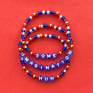 Peut inclure: Trois bracelets en perles avec des perles rouges, blanches et bleues. Les bracelets épellent "SOME IMAGINATION HUH" en lettres blanches sur des perles bleues.
