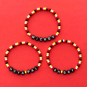 Peut inclure: Trois bracelets en perles avec des perles de lettres noires qui épellent "Mickey", "Hiya Pal" et "Oh Boy". Les perles sont rouges, jaunes et blanches.