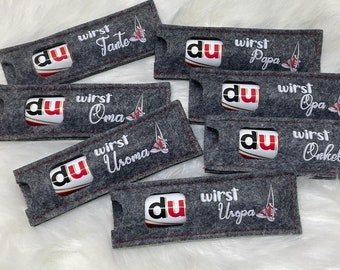 May include: Six gray felt gift bags with red and white accents. Each bag has a white embroidered design with the text "du wirst" followed by a German word, such as "Tante", "Oma", "Uroma", "Papa", "Opa", and "Onkel".