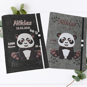 Könnte beinhalten: Zwei Babybücher aus Filz, eines in Dunkelgrau und eines in Hellgrau, jeweils mit einer Panda-Illustration. Die Bücher tragen den Namen "Niklas" und das Datum "12.02.2021" sowie das Gewicht des Babys in Gramm.