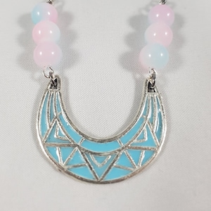 Könnte beinhalten: Eine silberne Halskette mit einem blauen und weißen geometrischen Anhänger und rosa und blauen Perlen.