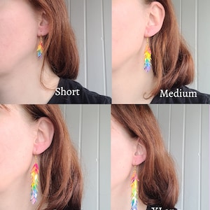 May include: Four pairs of rainbow-colored dangle earrings in different lengths: short, medium, long, and extra long. The earrings are made of iridescent plastic and have a gold hook.