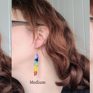 K&ouml;nnte beinhalten: Drei Paar Regenbogen-Ohrringe in verschiedenen Gr&ouml;&szlig;en: klein, mittel und gro&szlig;. Die Ohrringe bestehen aus schimmernden, &uuml;berlappenden Schuppen.
