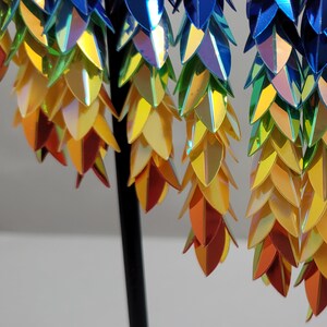 K&ouml;nnte beinhalten: Ein Paar regenbogenfarbene Ohrringe mit einem kaskadierenden Design aus blauen, gr&uuml;nen, gelben und orangefarbenen Schuppen.