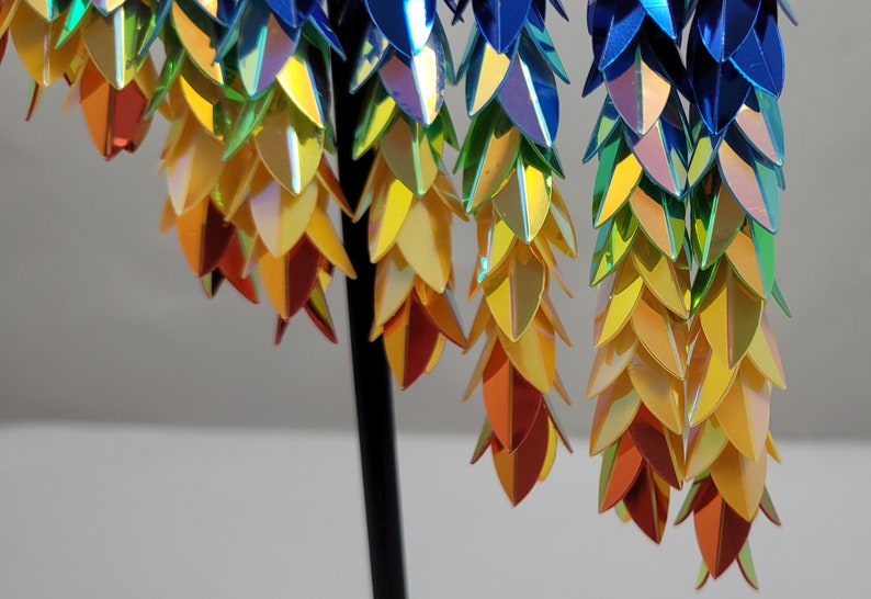 K&ouml;nnte beinhalten: Ein Paar regenbogenfarbene Ohrringe mit einem kaskadierenden Design aus blauen, gr&uuml;nen, gelben und orangefarbenen Schuppen.