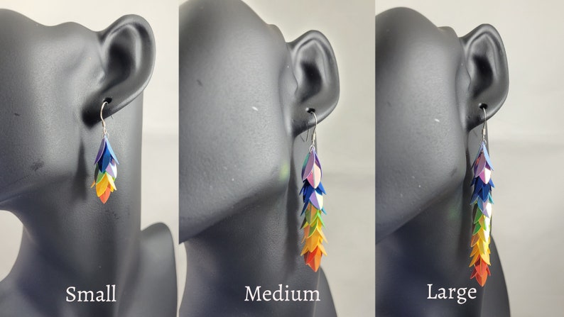 K&ouml;nnte beinhalten: Drei Paar Regenbogen-Ohrringe in verschiedenen Gr&ouml;&szlig;en: klein, mittel und gro&szlig;. Die Ohrringe sind aus Papier gefertigt und haben ein kaskadierendes Design aus bunten, schillernden Schuppen.