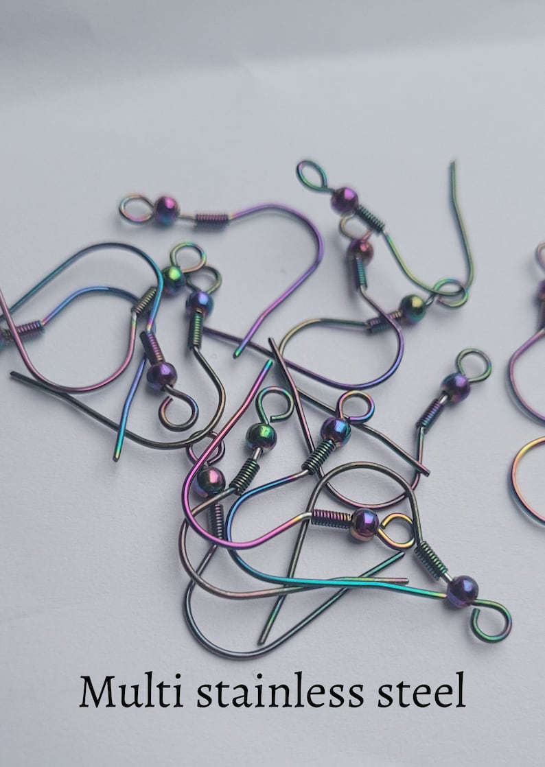 May include: A close-up of a pile of rainbow-colored stainless steel earring hooks. The hooks are all the same size and shape, and they are arranged in a random pattern. The hooks are made of a durable metal that is resistant to tarnishing.