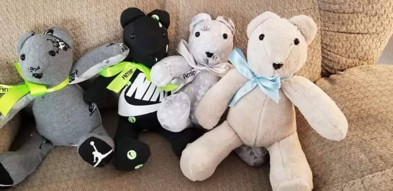 K&ouml;nnte beinhalten: Vier handgefertigte Teddyb&auml;ren in verschiedenen Farben, darunter Grau, Schwarz und Wei&szlig;. Die B&auml;ren haben Schleifen und B&auml;nder, und einige zeigen Nike-Logos und Details der Marke Jordan. Sie sitzen auf einem neutralfarbenen Sofa.