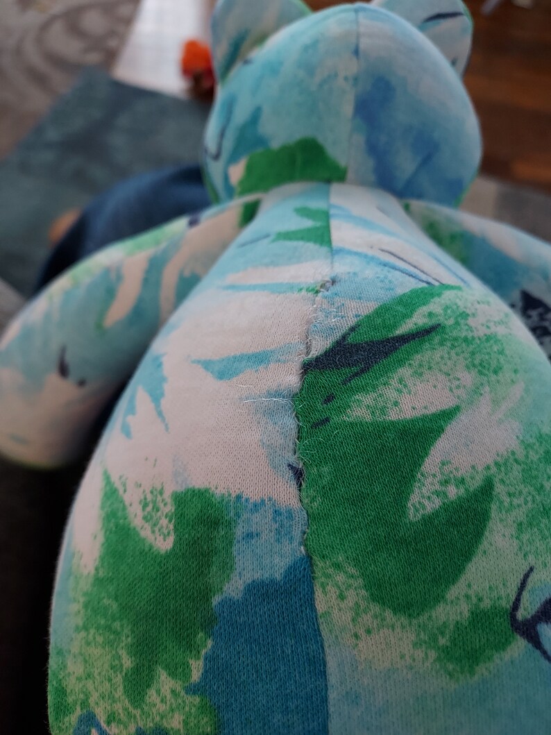 May include: A handmade stuffed animal in the shape of a frog. The frog is made of fabric with a pattern of blue, green, and white abstract shapes. The stitching is visible along the seams.