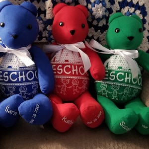 May include: Three colorful handmade teddy bears: blue, red, and green. Each bear has a white ribbon, black button eyes, and the word "Preschool" printed on its belly. The bears' feet are embroidered with names and dates.