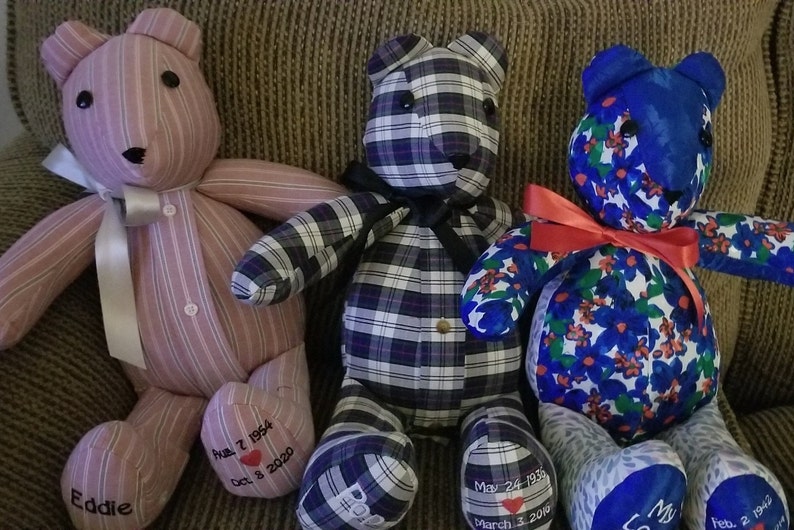 May include: Three handmade teddy bears with unique fabric patterns. One is pink striped, another is black and white plaid, and the third is blue with floral designs. Each bear has a ribbon and embroidered details, including dates and names.