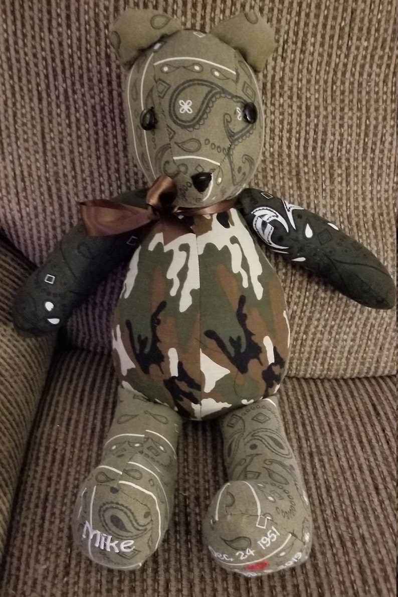 May include: A handmade teddy bear with a camouflage body and paisley patterned head, arms, and legs. The bear has black button eyes and a brown ribbon bow. The bear's foot reads "Mike" and "Dec. 24 1951".