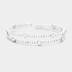 May include: A silver double-row bangle bracelet with clear rhinestones. The bracelet has a delicate design with small, round stones.