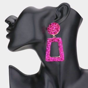 May include: A pair of pink statement earrings with a geometric design. The earrings are made of rhinestones and have a gold-tone finish.