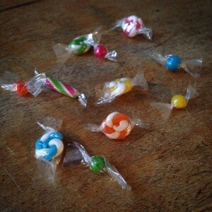 May include: Assortment of wrapped sweets in various colours and designs, including a striped candy cane, a swirl sweet, and a sweet with a yellow and white design.