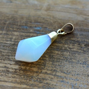 May include: A white opal pendant with a gold setting. The opal is faceted and has a teardrop shape.