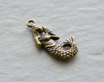 May include: A bronze mermaid charm featuring a detailed design. The mermaid is shown with flowing hair and a scaly tail.